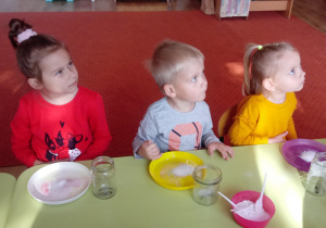 Dzieci siedzą przy stoliku i słuchają polecenia